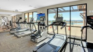A gym with treadmills, ellipticals, and a large window with a view of the beach. - SeaChase 1601W by Liquid Life (Orange Beach)