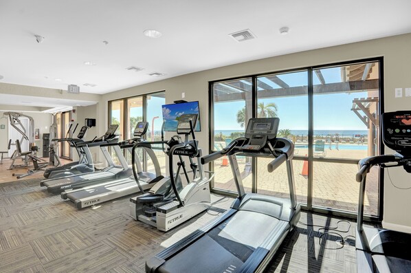 A gym with treadmills, ellipticals, and a large window with a view of the beach.