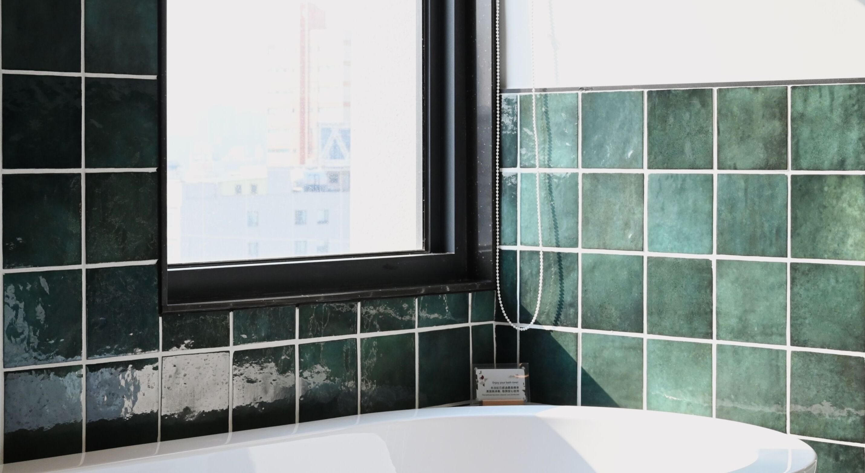 A bathroom with a bathtub, a window, and green tiled walls.
