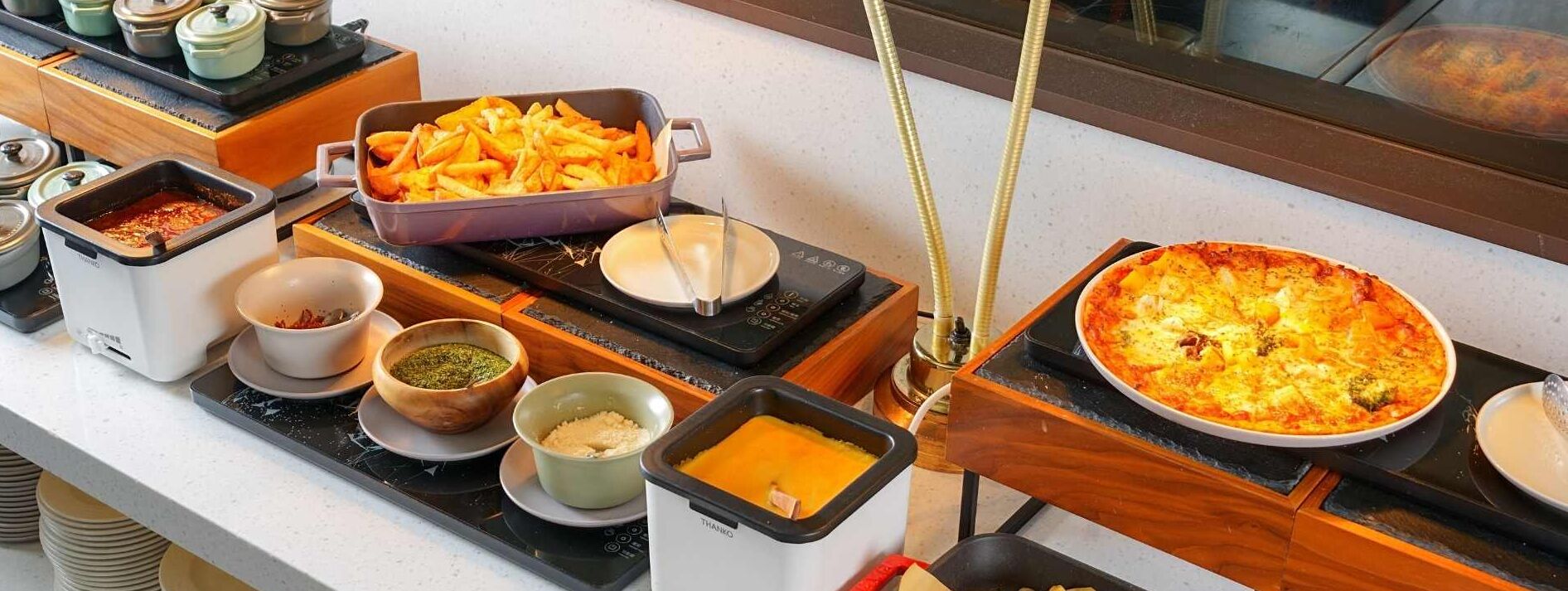 A buffet setup with various dishes including fries, a pizza, and different sauces.
