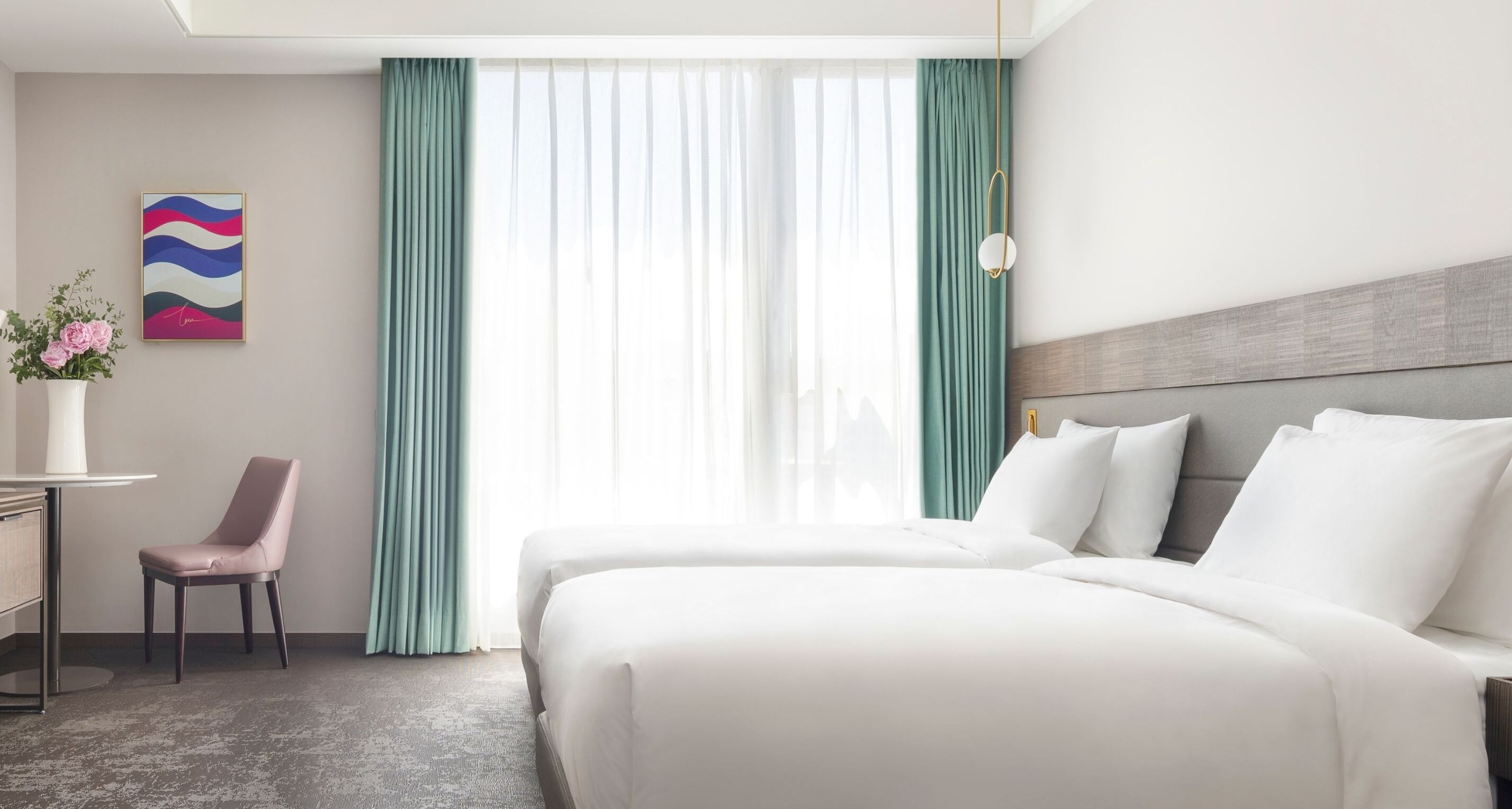 A hotel room with two beds, a desk, a chair, and a window with curtains.