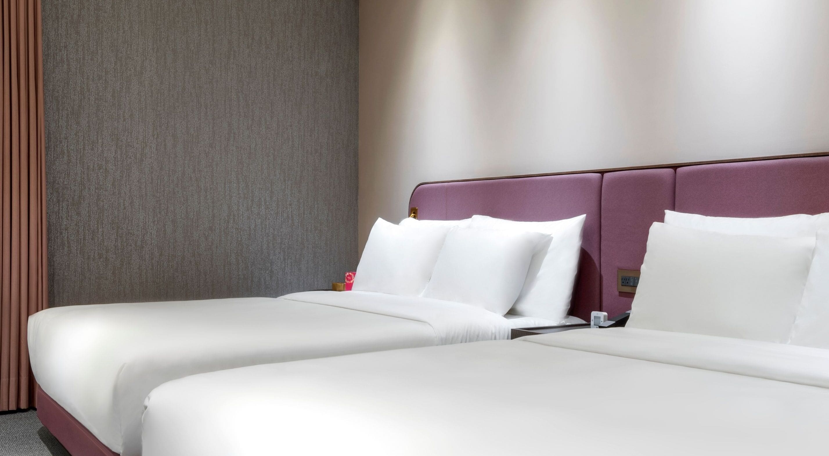 Een hotelkamer met twee bedden, een gestructureerde grijze muur en een paars hoofdeinde.