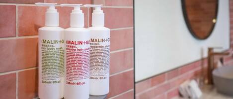 Three bottles of MALIN+GO hair conditioner on a shelf against a brick wall.