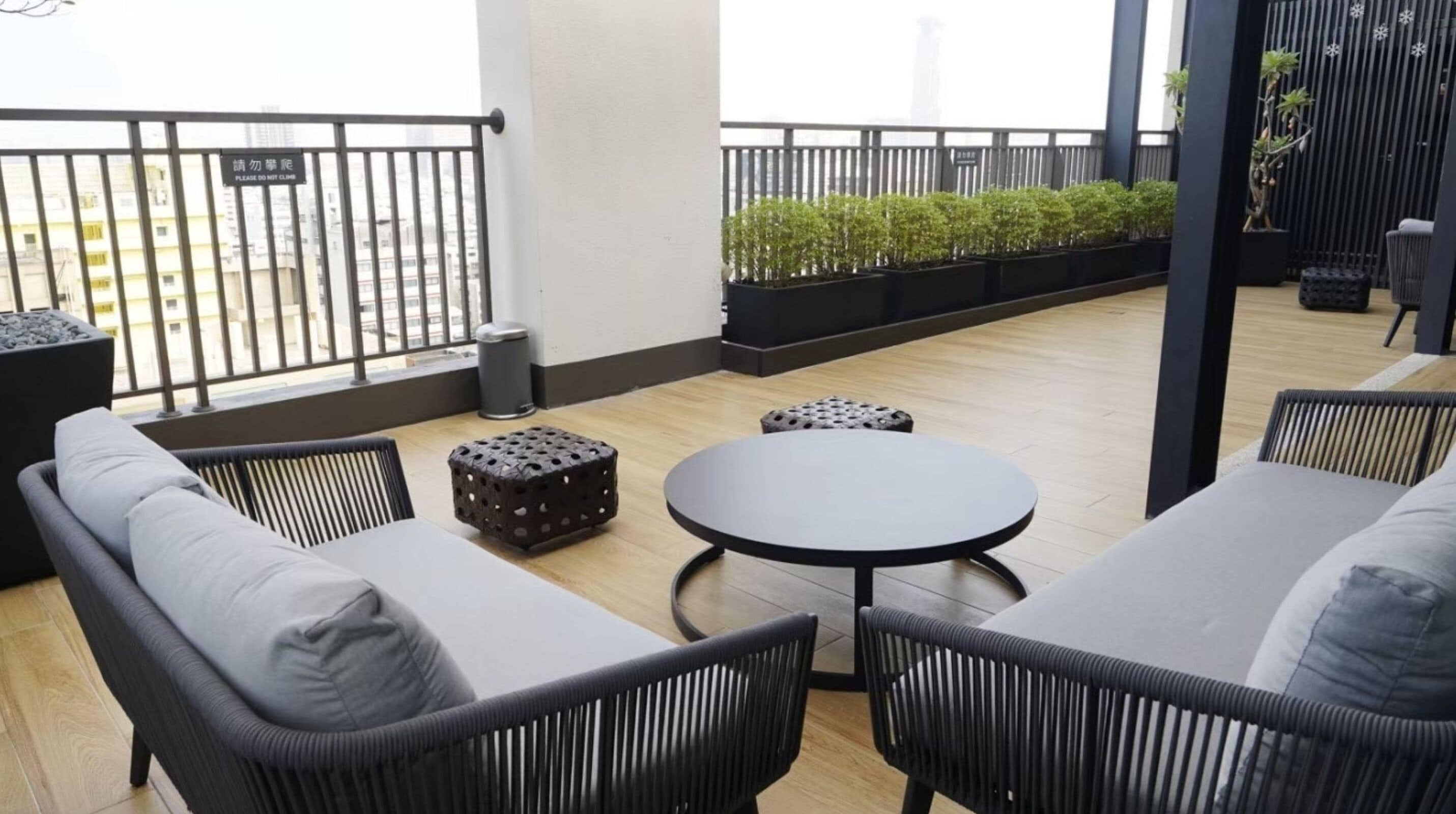 Un balcon agrémenté de meubles en osier noir, d’une table ronde et de plantes en pot.