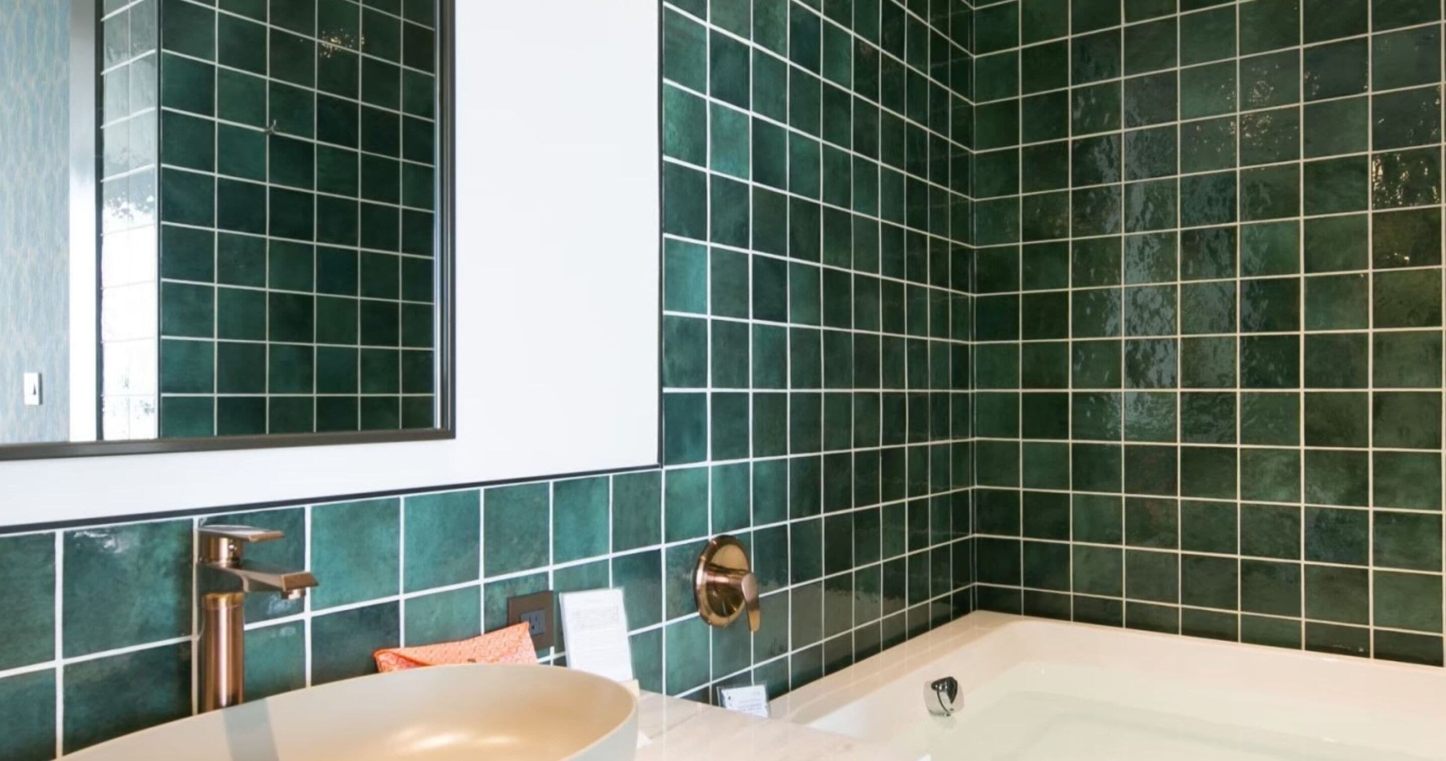 A bathroom with a large bathtub, a sink, and a mirror. The walls are tiled with green tiles.