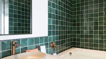 A bathroom with a large bathtub, a sink, and a mirror. The walls are tiled with green tiles.