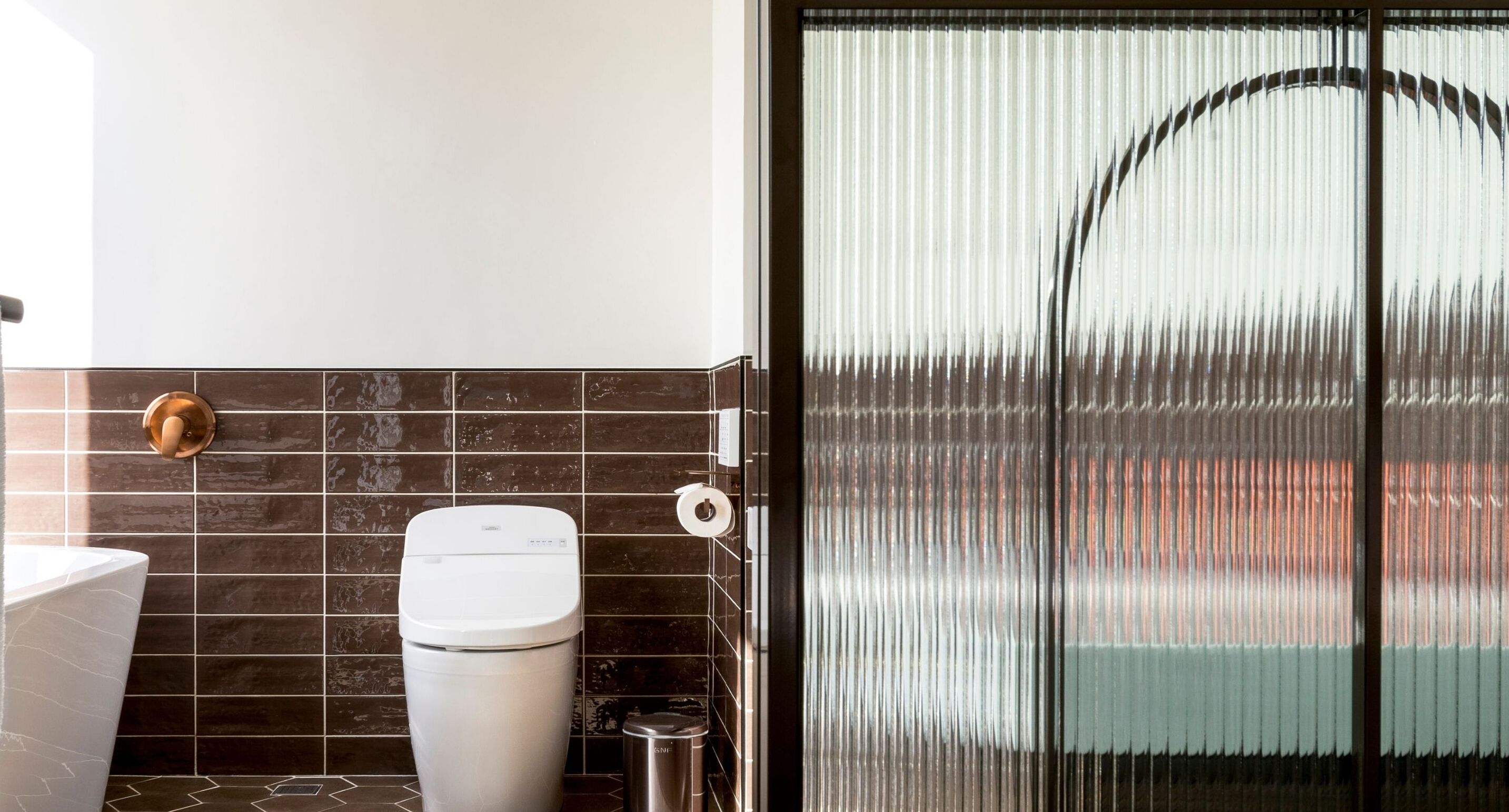 A bathroom with a toilet, a trash bin, and a shower area with a glass door.