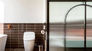 A bathroom with a toilet, a trash bin, and a shower area with a glass door.