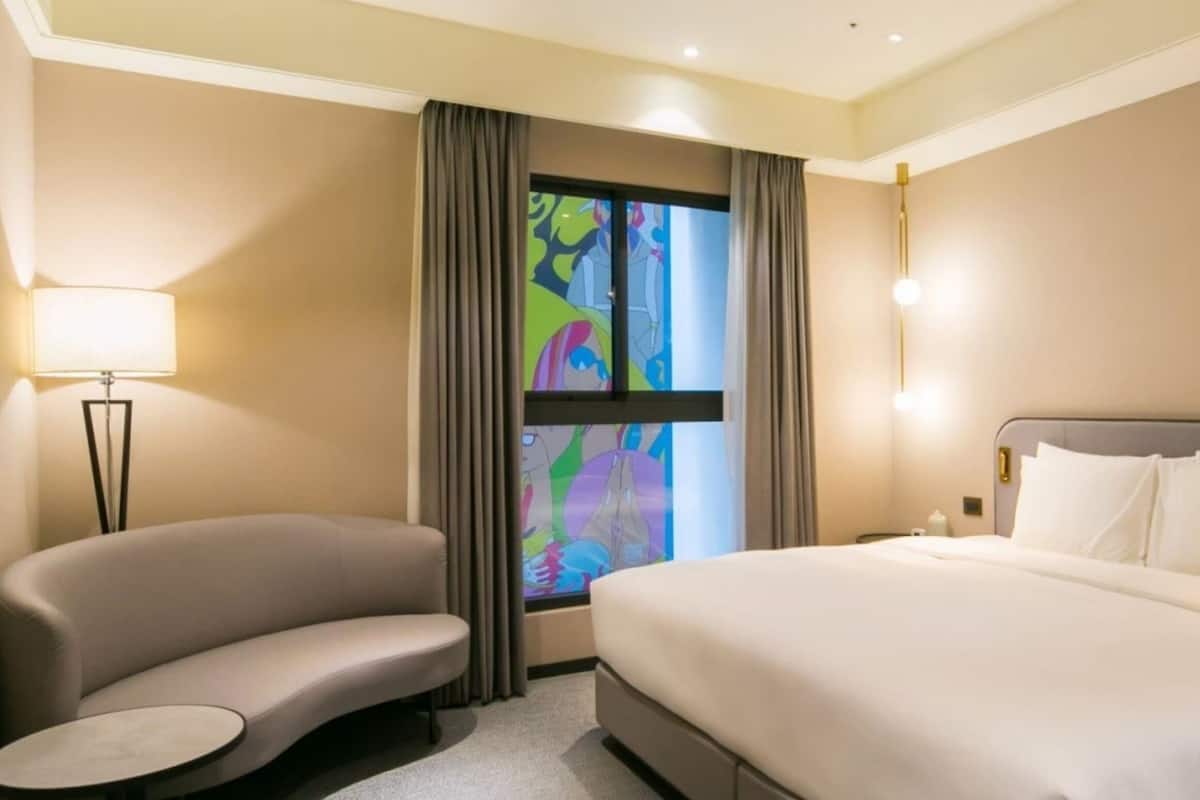 Una habitación de hotel con cama, sofá, una mesita y ventana con cortinas.