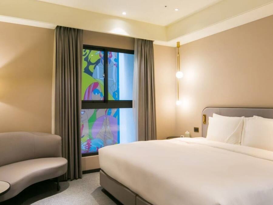 A hotel room with a bed, a sofa, a small table, and a window with curtains.