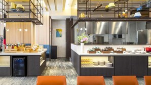 Un restaurante moderno con cocina central, zona de comedor con sillas naranjas y un entrepiso con asientos.