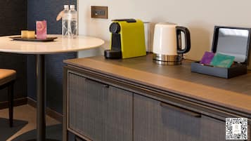 A hotel room with a round table, a minibar, a kettle, and a small cabinet.
