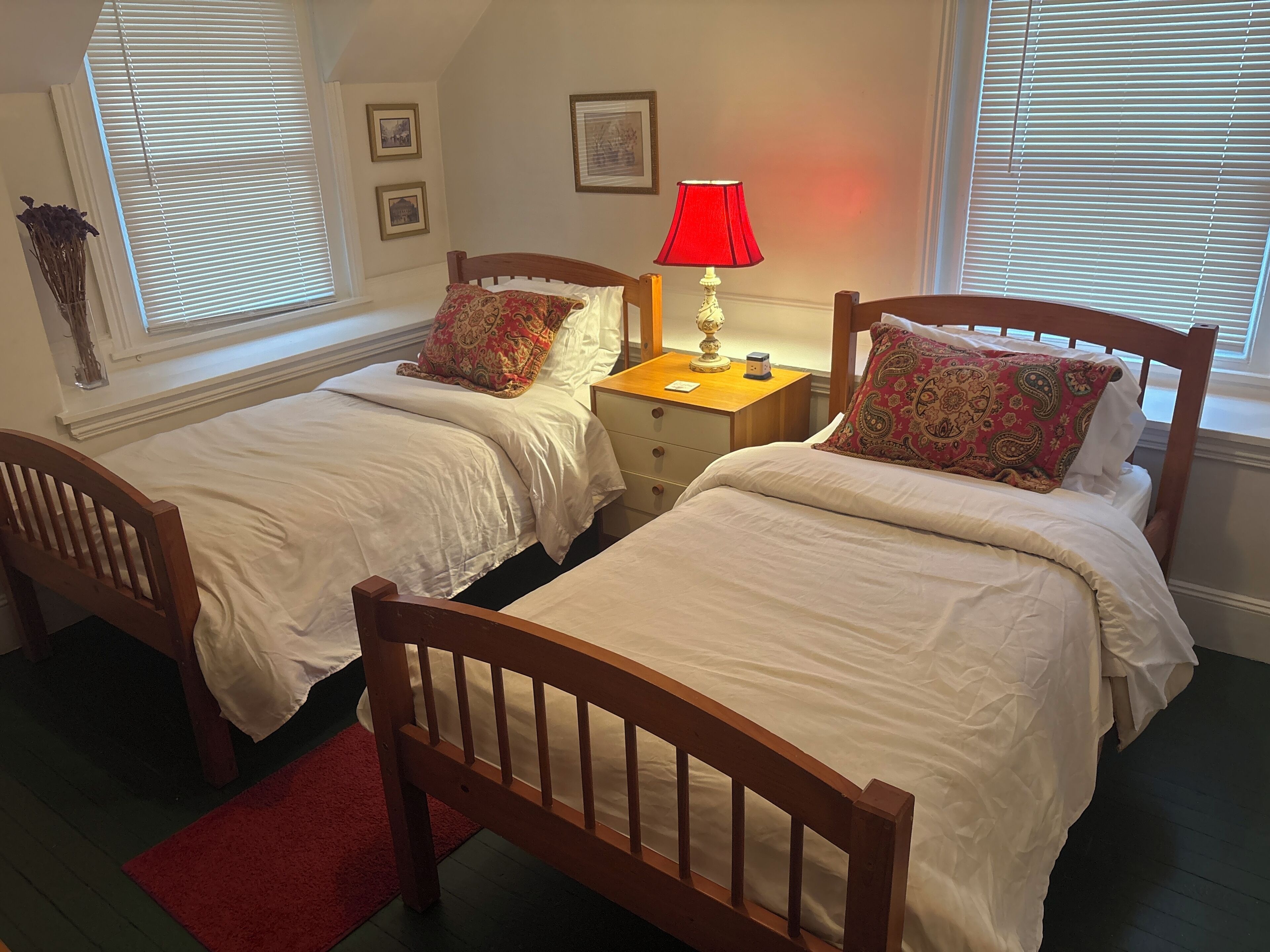 A bedroom with two wooden beds, a nightstand with a lamp, and a red rug.