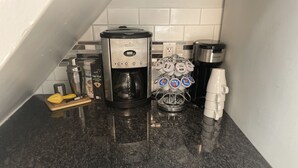 Una encimera de cocina con una cafetera, un exprimidor, un molinillo de café y un portavasos.