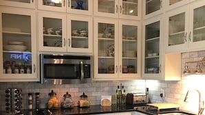 Una cocina con armarios blancos, encimera negra, microondas de acero inoxidable, horno y fregadero.