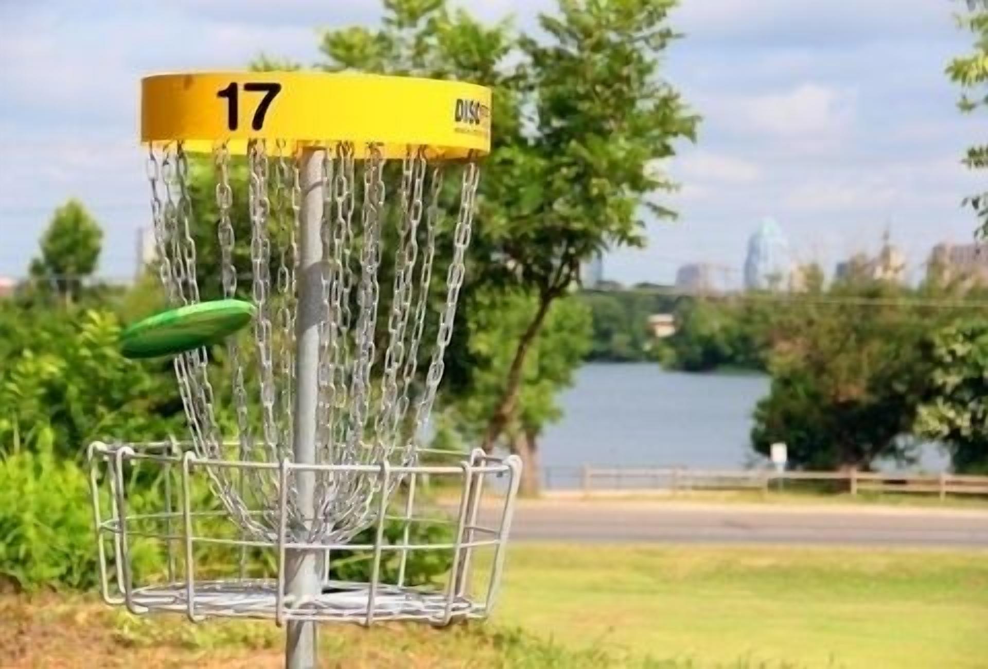 A disc golf basket with a yellow disc on it, number 17, and a chain-link fence in the foreground.