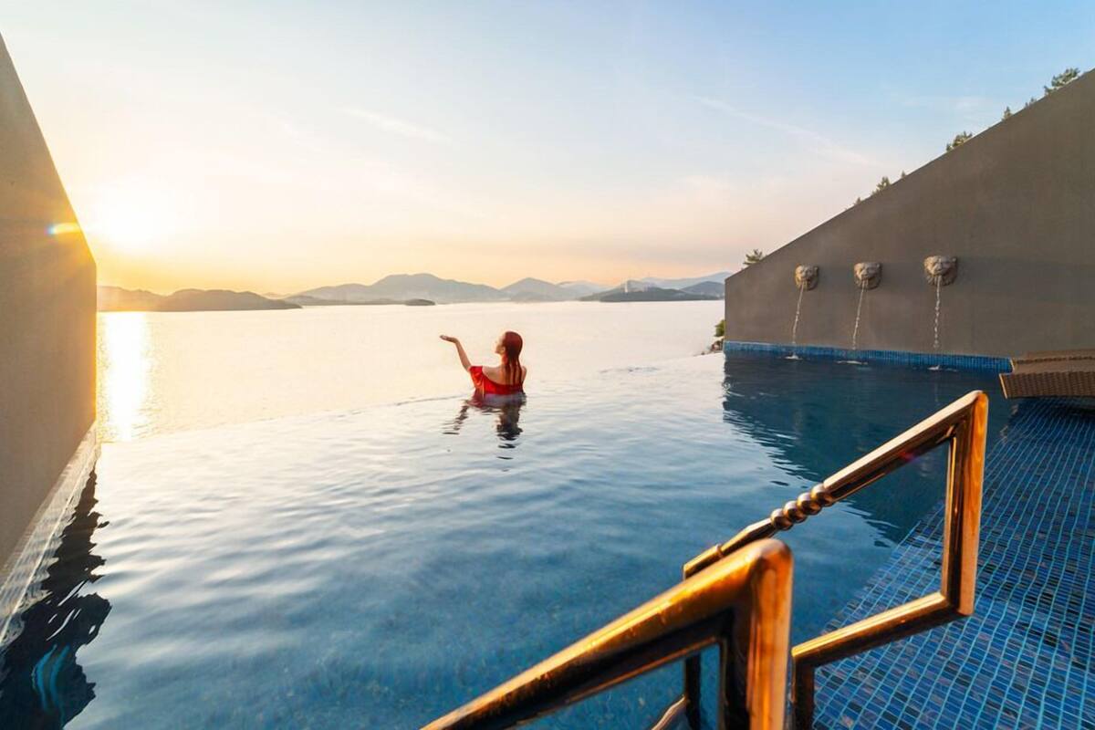 A person in a red swimsuit in a pool with a sunset view, a blue tiled deck, and a concrete wall with three lion statues.