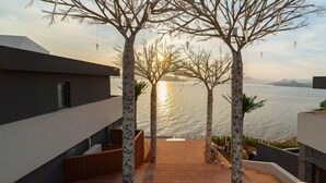 Un bâtiment moderne doté d’une terrasse en bois qui mène à un balcon offrant une vue sur une étendue d’eau.