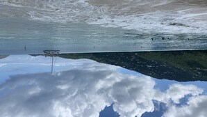 A beach with waves, a clear sky, and a reflection of clouds in the water.