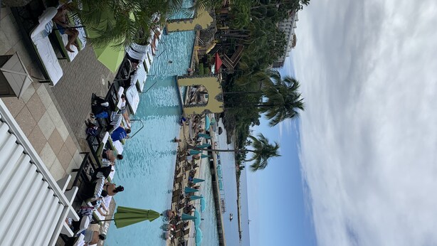 A pool area with lounge chairs and umbrellas, a beach area with sun loungers, and a view of the ocean.