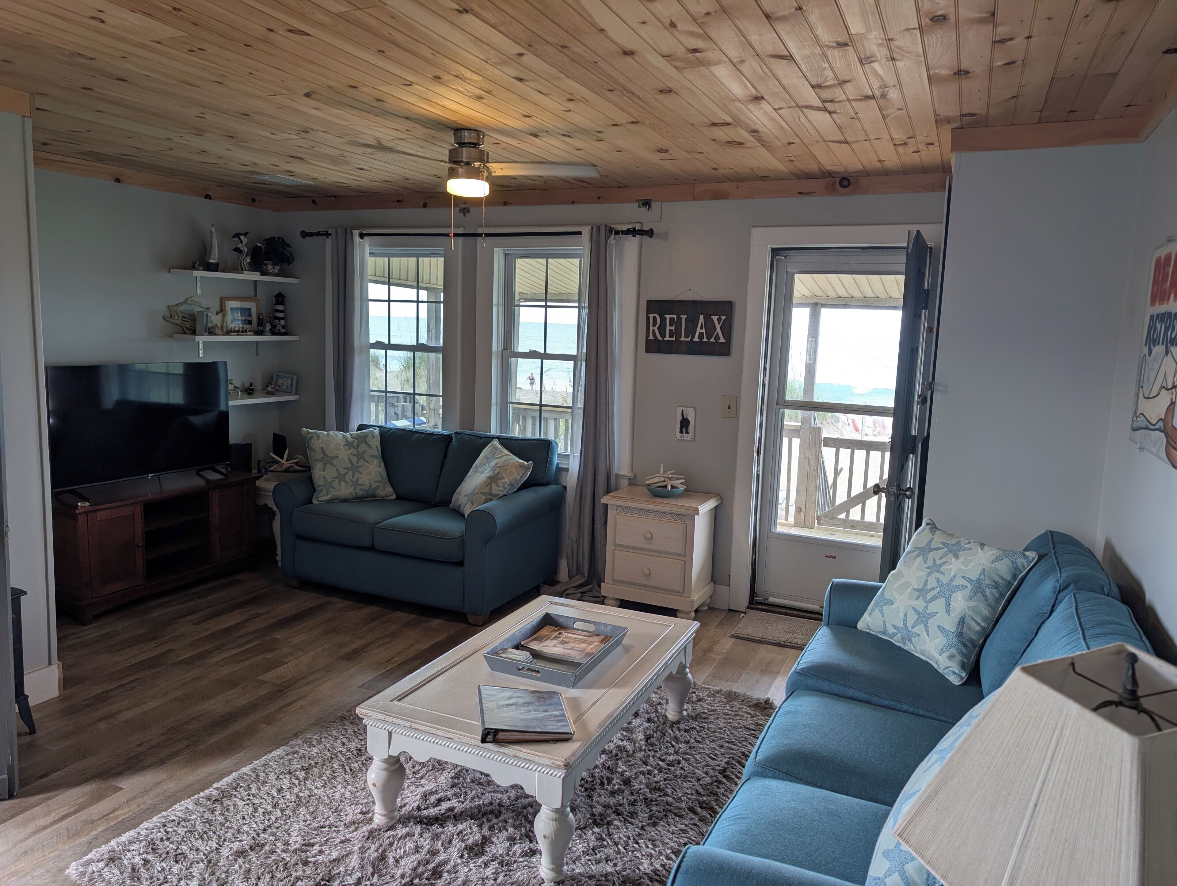 Un salon avec un téléviseur, un canapé bleu, un plancher en bois et un ventilateur de plafond.