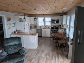 A compact kitchen with white cabinets, a wooden ceiling, and a dining area with a table and chairs. - Beach Retreat - OceanFront Cottage (Kitty Hawk)