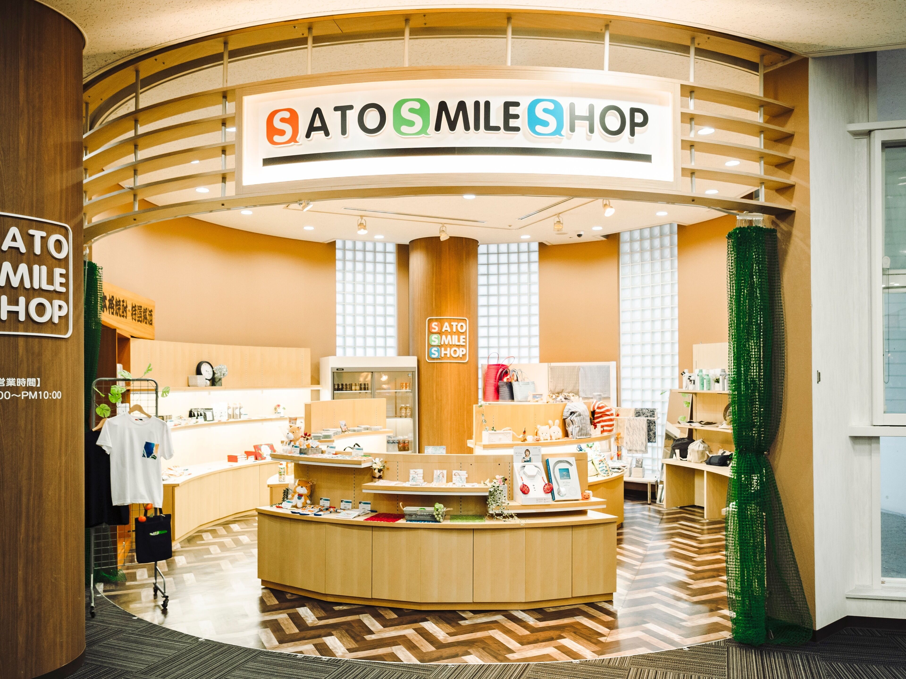 Botiga amb un taulell de fusta corbat i un cartell que diu "SATO SMILE SHOP".