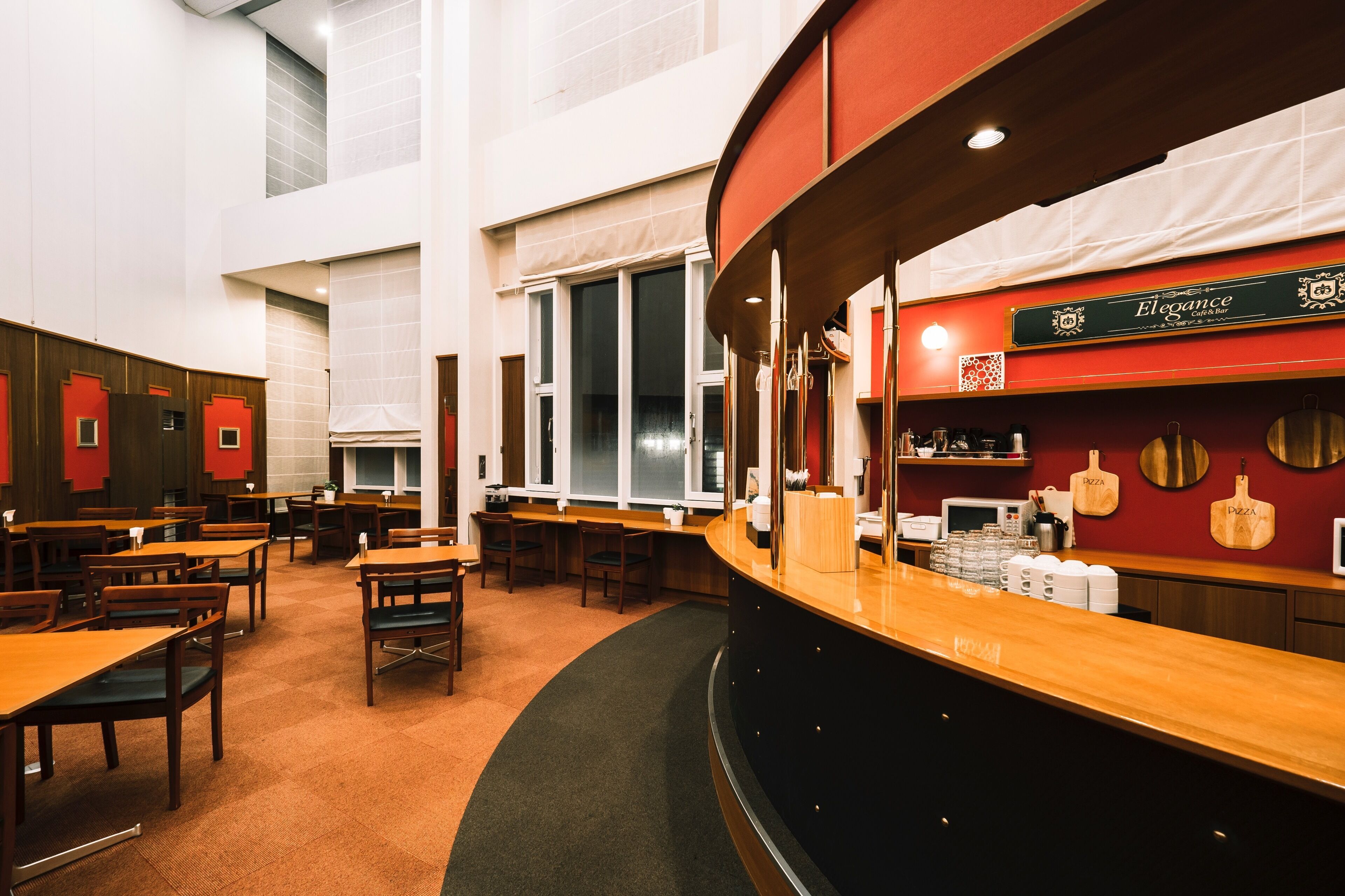 A restaurant with a curved counter, wooden tables, and chairs. There are large windows and a sign that reads "Elegance Cafe & Bar".