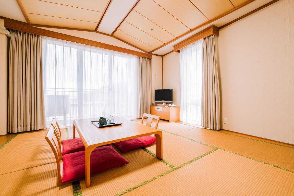 A traditional Japanese room with tatami flooring, a low table with cushions, a television, and sliding doors.