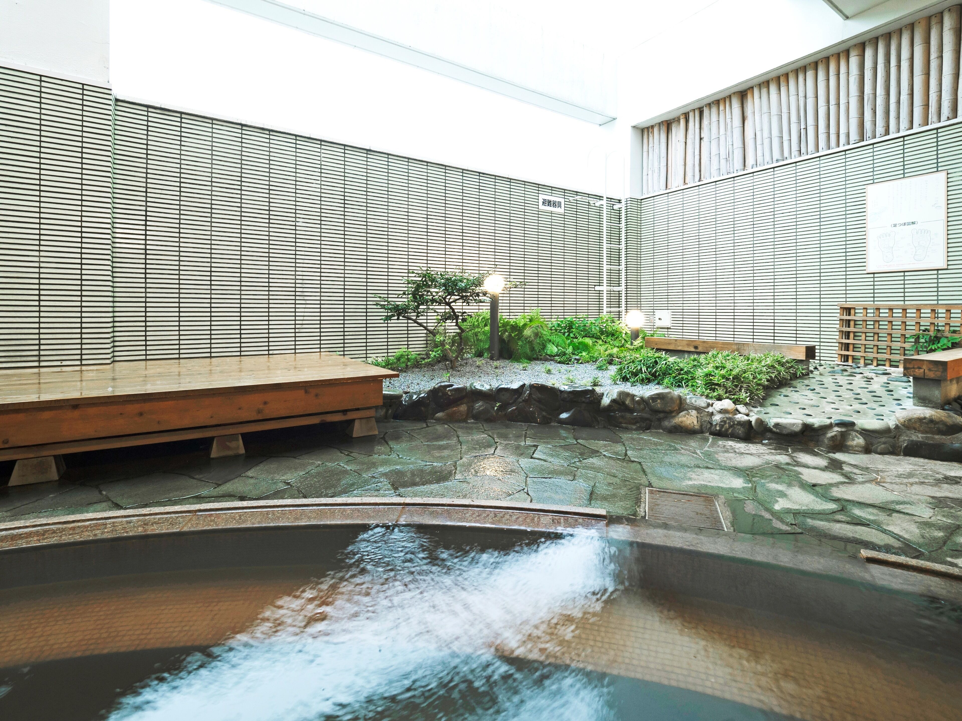 Un onsen japonais traditionnel, avec un banc en bois, un sentier de pierres et une petite cascade.