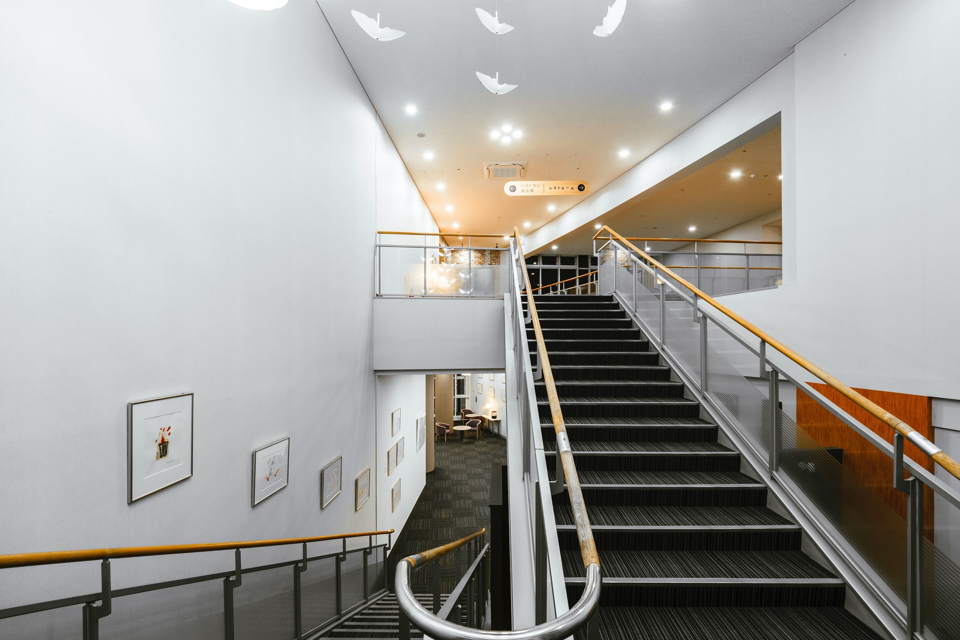 A modern interior with a staircase, glass railings, and framed artwork on the walls.