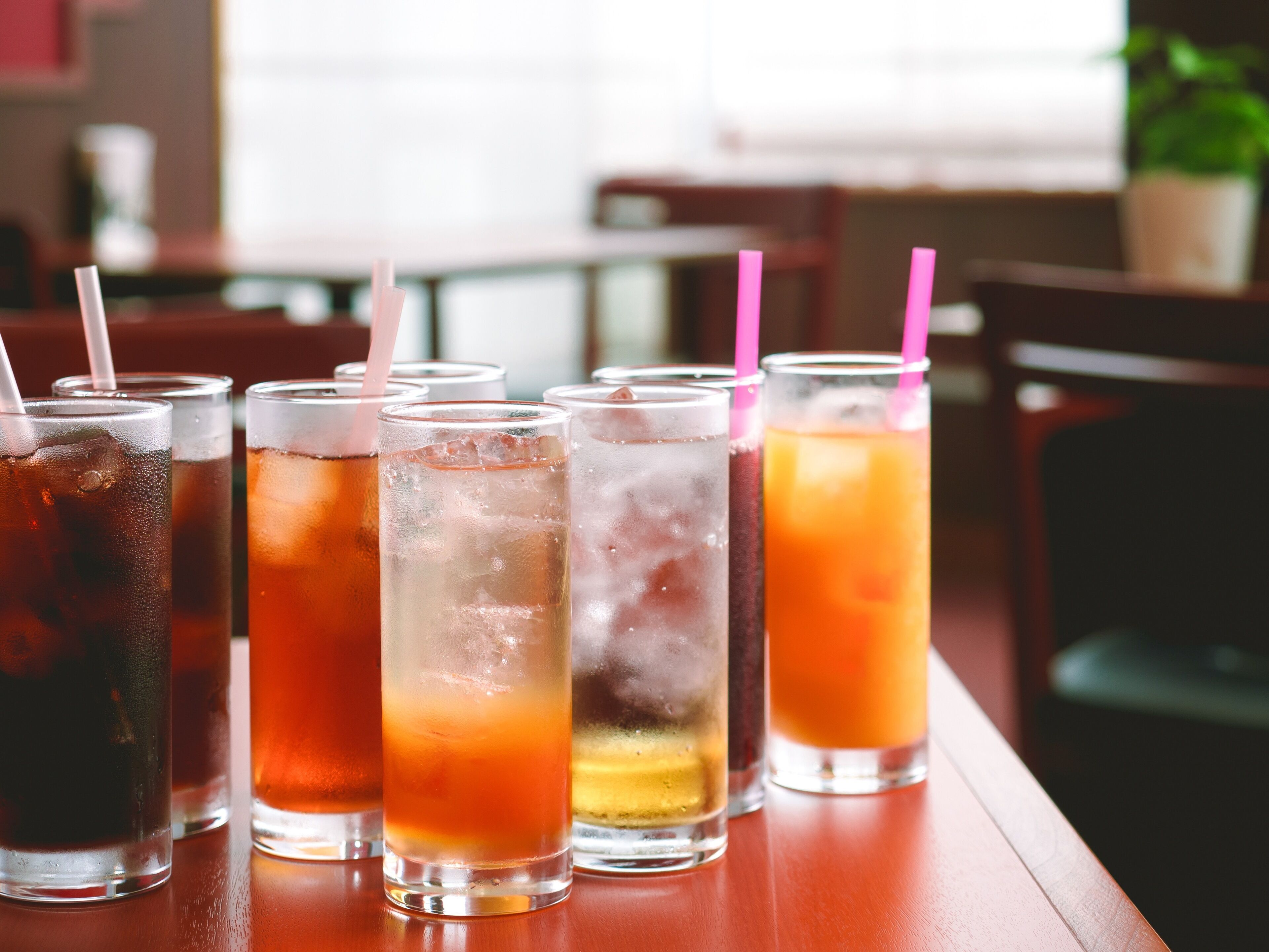 A row of iced drinks with straws on a wooden table.