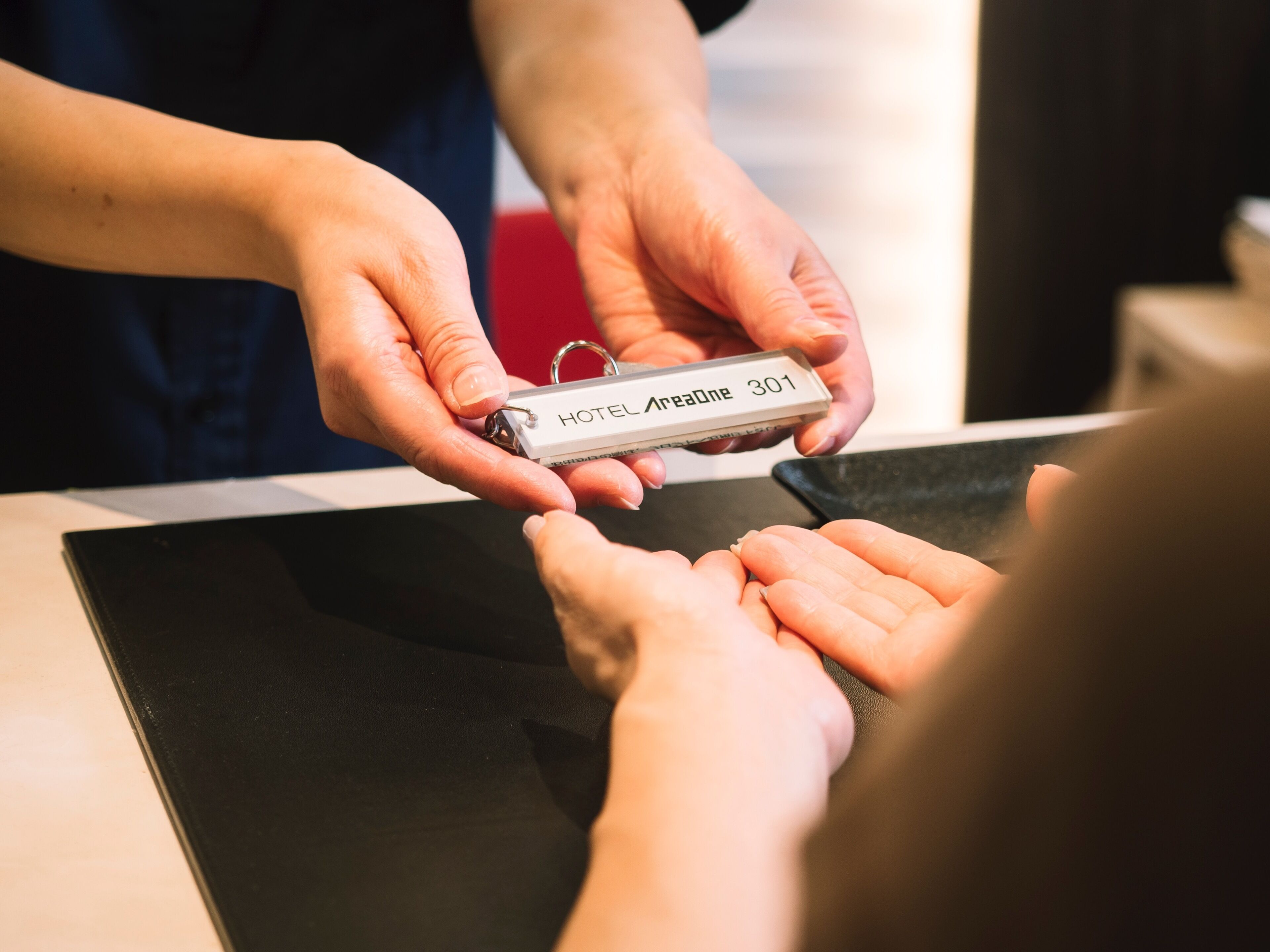 A person handing over a key labeled "HOTEL AreaOne 301" to another person.