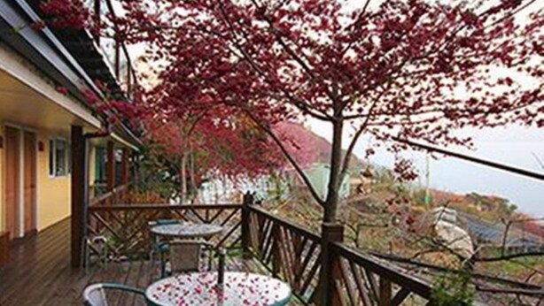 A wooden deck with two round tables and chairs, a railing, and a view of the landscape. - Chingjing New Paradise B&B (Ren'ai)