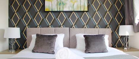 Relax in a stylish room with a large bed, geometric patterned wall, and a framed painting.