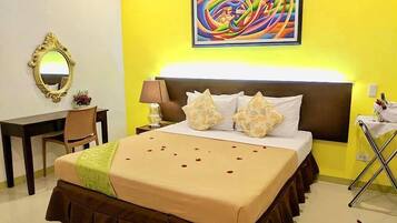Habitación de hotel con cama, escritorio, silla, lámpara y un cuadro en la pared.