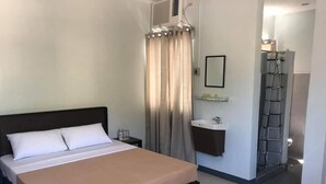 Et hotelværelse med en seng, et natbord med lampe, et badeværelse med håndvask og spejl, samt et bruseområde.