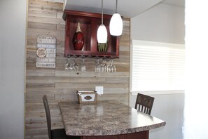 Kitchen area with a granite countertop, wooden shelf, and wine glasses.