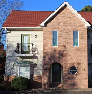 Une maison à deux étages avec une façade en briques, un toit rouge et une porte verte.