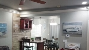 A living room with a dark leather couch, a coffee table with magazines, a dining area with a glass table and chairs, a kitchen with wooden cabinets, and a ceiling fan. - Beautiful Lake View Condo. Minutes to Racetrack (Hot Springs)