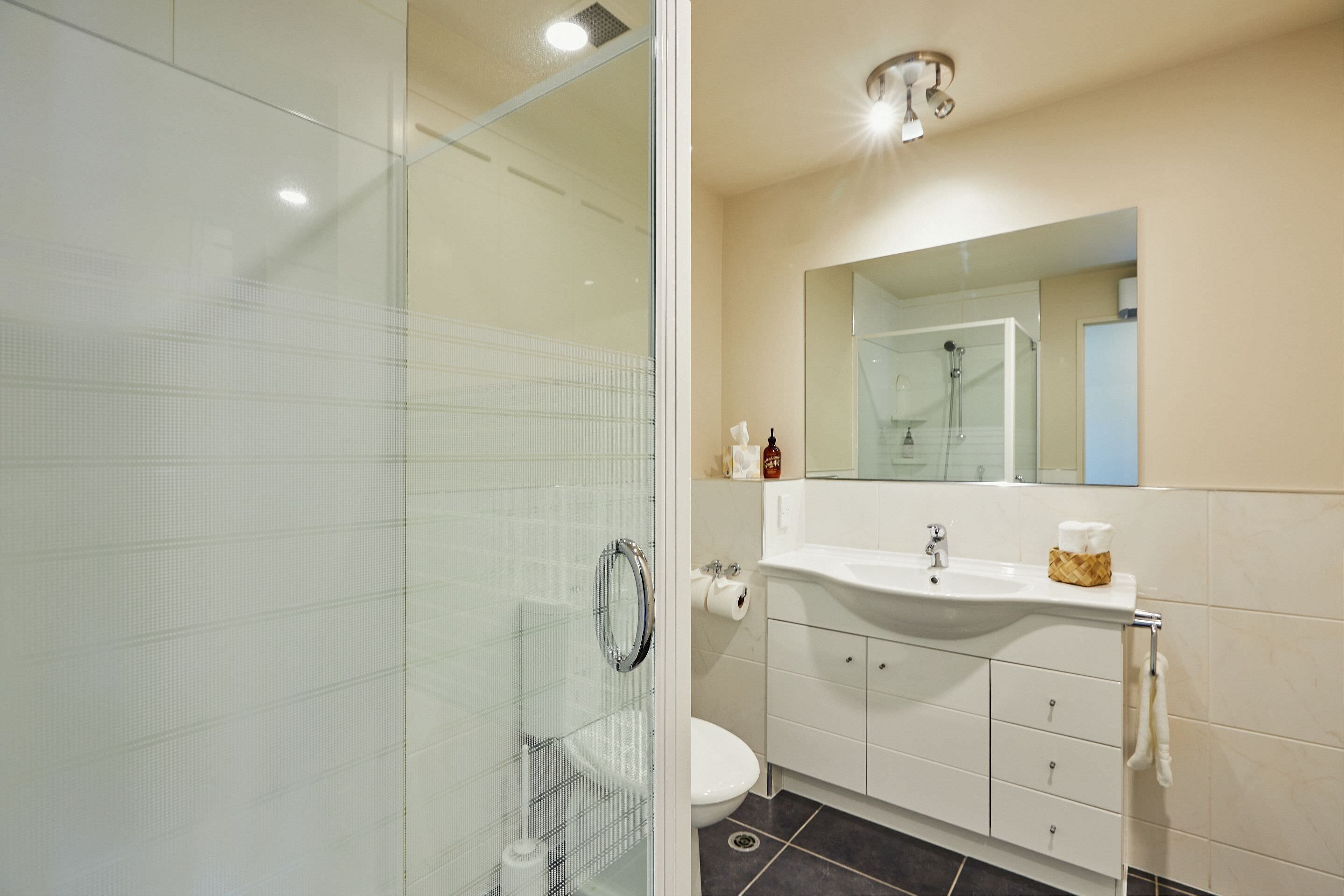 A modern bathroom with a glass shower enclosure, a white sink with a mirror above, and a toilet.