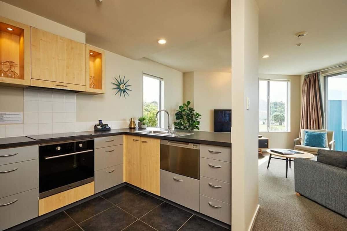 A modern kitchen with grey cabinets, a dishwasher, and a sink. There is a dining area with a grey sofa and a small table.