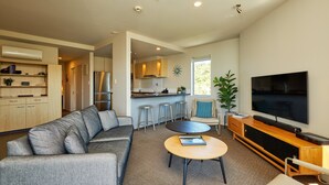 Ein modernes Wohnzimmer mit grauem Sofa, einem Couchtisch, einem Fernseher und einer Küchenzeile mit Barhocker.