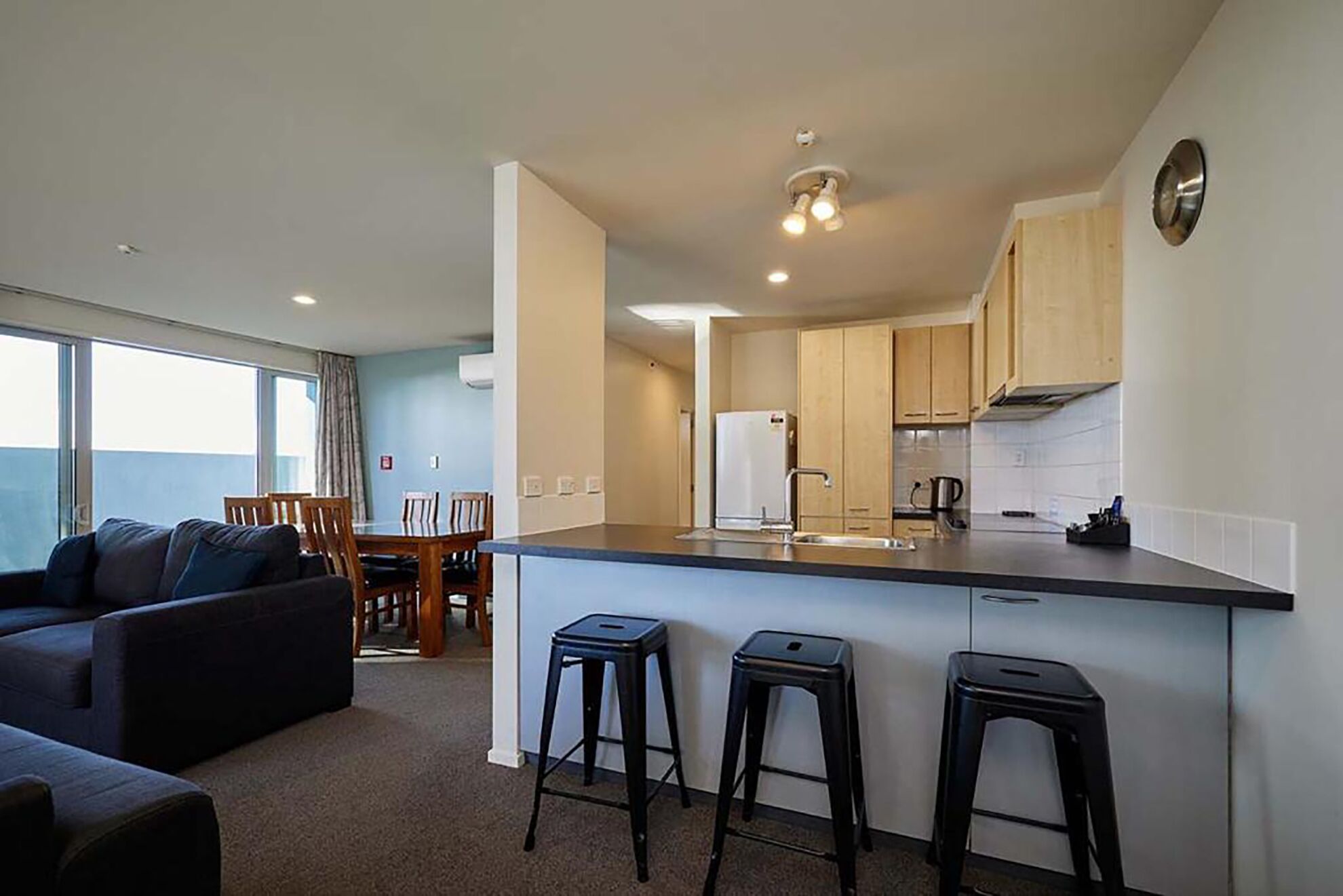 Una cocina moderna con una isla central, taburetes de bar y un comedor con mesa y sillas.