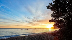 Ein Strand mit Sonnenuntergang, ruhiger See und Bäumern am Horizont.
