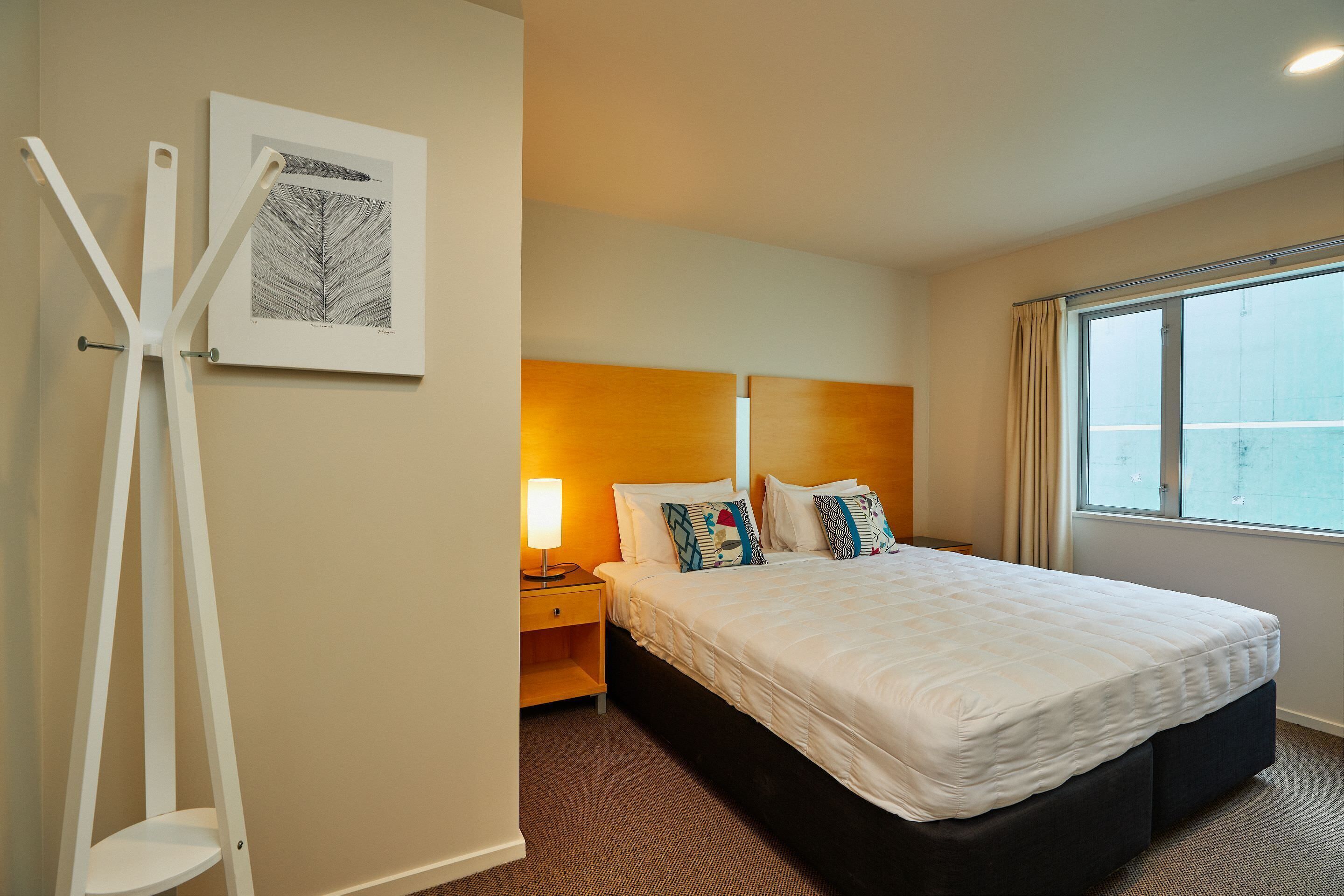 A hotel room with a large bed, a bedside table with a lamp, a wall-mounted artwork, and a window with curtains.