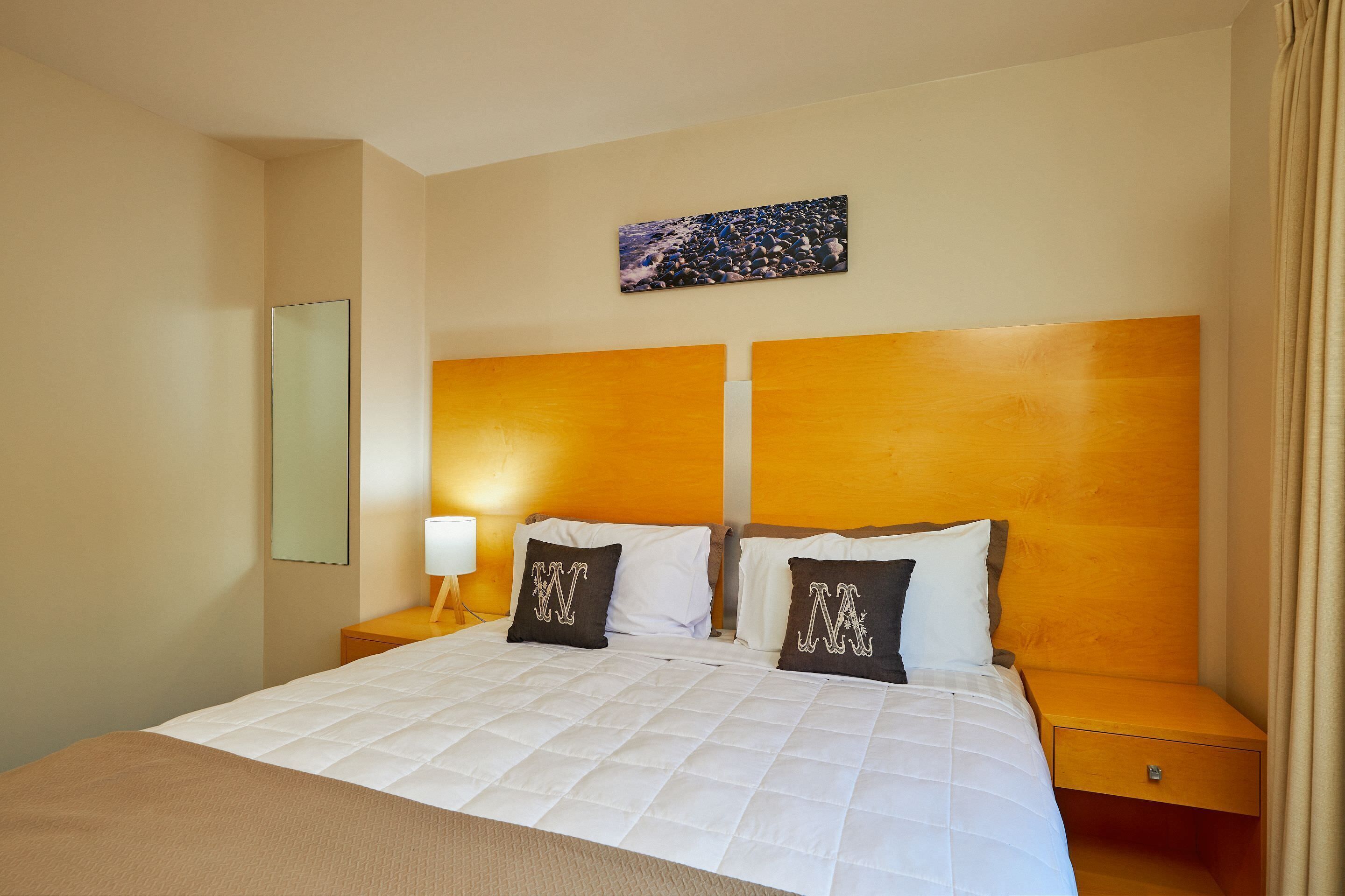 A hotel room with a large bed, two nightstands, a bedside lamp, a painting on the wall, and a mirror.
