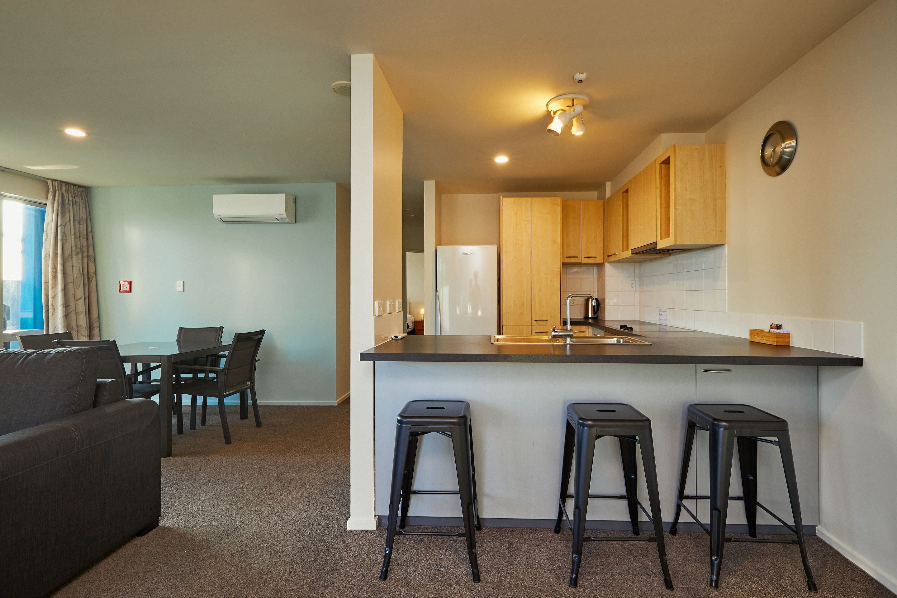 Een moderne keuken met houten kastjes, een centraal eiland met krukken, en een zithoek met een bank en stoelen.