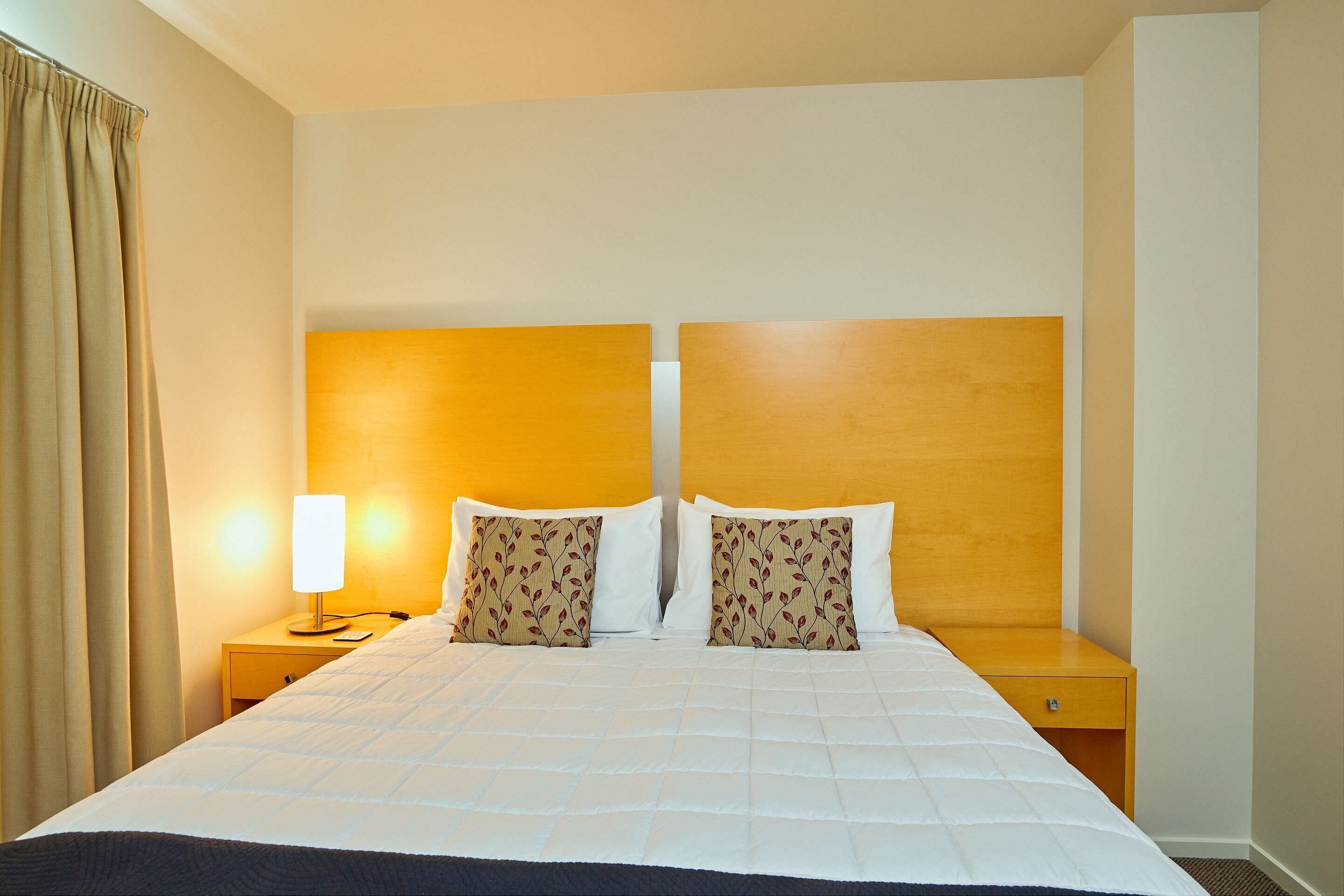 A hotel room with a large bed, two nightstands, a lamp, and a curtain.
