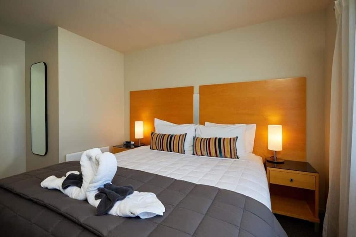 A neatly made bed with a dark brown headboard, two bedside lamps, and a mirror on the wall.